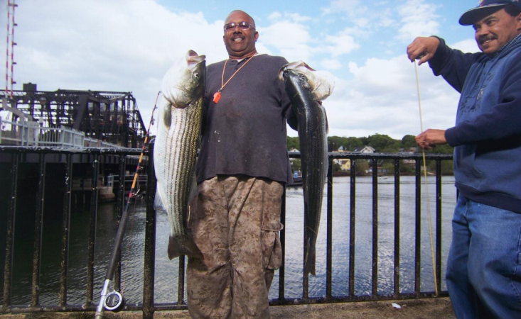 Man proudly holding two large fish by a waterfront