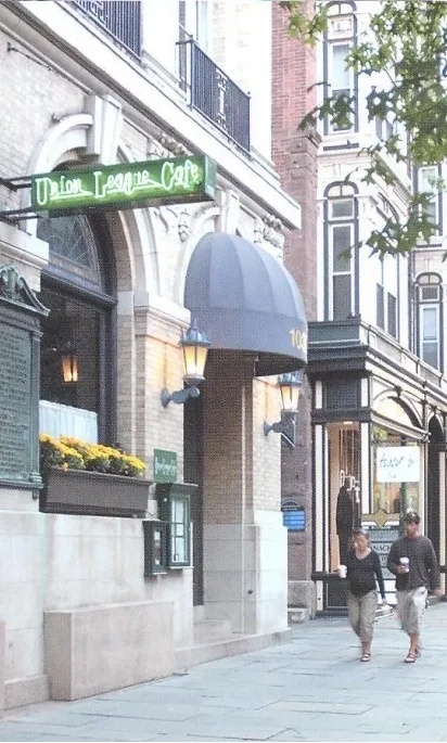 A person walking on a city sidewalk past a building with a green street sign